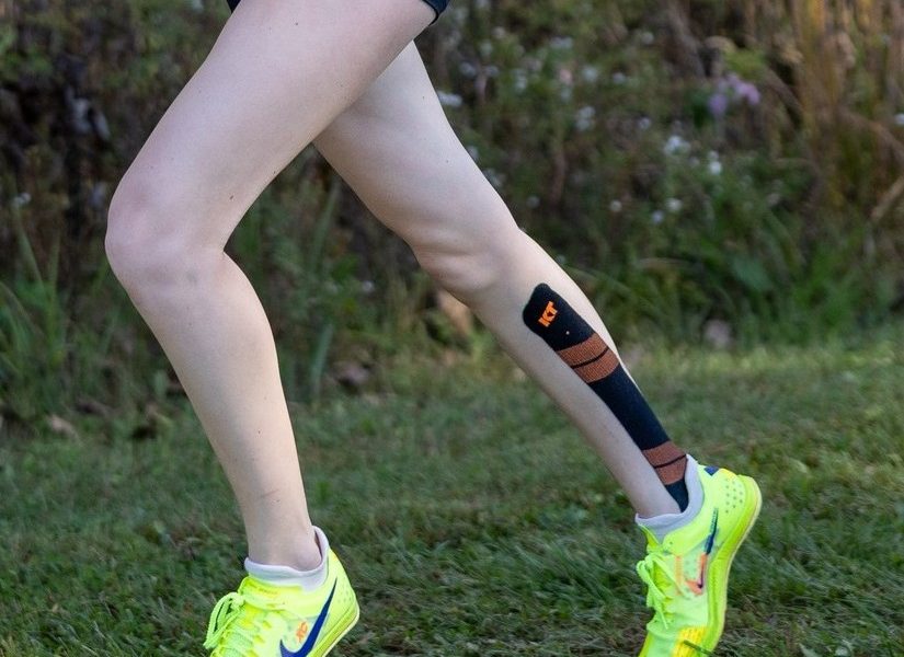 Legs of a female running on a grass course wearing spikes.