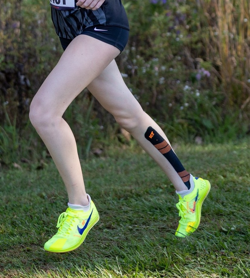 Legs of a female running on a grass course wearing spikes.